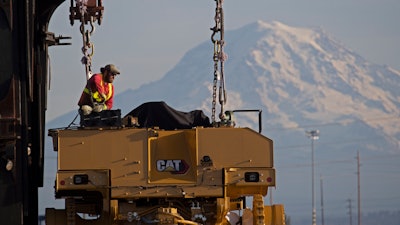 In this Nov. 4, 2019 photo, a worker prepares a piece of Cat construction equipment made by Caterpillar to be lifted off a trailer at the Port of Tacoma in Tacoma, WA.