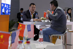 In this Nov. 6, 2019 file photo, visitors chat near American and Chinese flags displayed at a booth for an American company promoting environmental sensors during the China International Import Expo in Shanghai.
