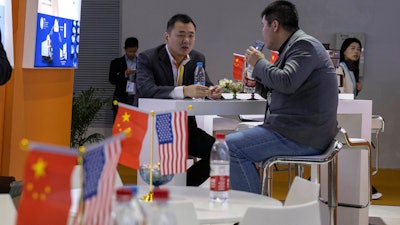 In this Nov. 6, 2019 file photo, visitors chat near American and Chinese flags displayed at a booth for an American company promoting environmental sensors during the China International Import Expo in Shanghai.