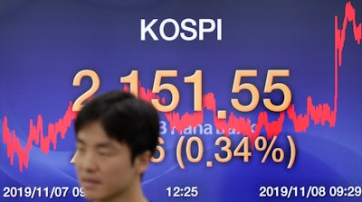 A currency trader walks by the screen showing the Korea Composite Stock Price Index (KOSPI) at the foreign exchange dealing room in Seoul, South Korea on Friday, Nov. 8.