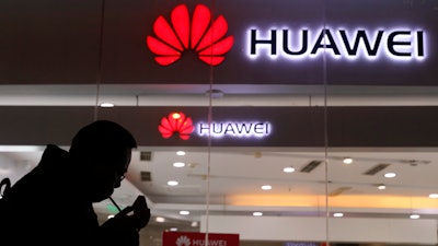 In this Dec. 6, 2018 file photo, a man lights a cigarette outside a Huawei retail shop in Beijing.