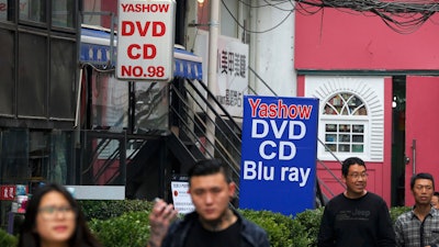 In this April 27, 2016 file photo, people walk past a shop selling pirated movie DVDs and music CDs in Beijing.