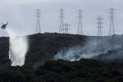 In this Oct. 10, 2019, file photo, a helicopter drops water near power lines and electrical towers while working at a fire on San Bruno Mountain near Brisbane, Calif. California’s Pacific Gas & Electric is faced regularly with a no-win choice between risking the start of a deadly wildfire or immiserating millions of paying customers by shutting off the power.