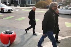 Piaggio Fast Forward CEO Greg Lynn, center, is followed by his company's Gita carrier robot as he crosses a street on Monday, Nov. 11, in Boston. The two-wheeled machine is carrying a backpack and uses cameras and sensors to track its owner.