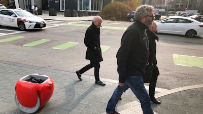 Piaggio Fast Forward CEO Greg Lynn, center, is followed by his company's Gita carrier robot as he crosses a street on Monday, Nov. 11, in Boston. The two-wheeled machine is carrying a backpack and uses cameras and sensors to track its owner.