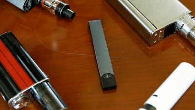 This Tuesday, April 10, 2018 file photo shows vaping devices, including a Juul, center, that were confiscated from students at a high school in Marshfield, MA.