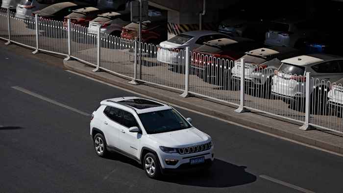 In this March 14, 2019, file photo, an SUV moves past dust-covered new Toyota cars stored underneath an overpass in Beijing. China's auto sales sank 5.4% in November from a year ago, putting the industry's biggest global market on track to shrink for a second year, an industry group reported Tues, Dec. 10, 2019. Drivers bought just over 2 million SUVs, sedans and minivans, according to the China Association of Automobile Manufacturers.