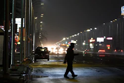 In this May 2, 2019, file photo, a pedestrian crosses Gratiot Street at Outer Drive East under a bright streetlight flanked by dimmer streetlights in Detroit. Leotek Electronics USA has agreed to pay $4 million to settle a lawsuit with Detroit over thousands of defective streetlights in Detroit, a newspaper reported. The city sued the company last spring, alleging that roughly 20,000 lights were failing.