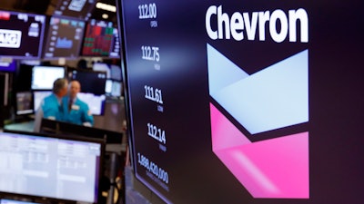 This Oct. 8, 2019, file photo shows the logo for Chevron on the floor of the New York Stock Exchange. Chevron Corp. reports financial results Friday, Nov. 1. Chevron said Tuesday, Dec. 10, it will book a charge of at least $10 billion because lower long-term prices for oil and natural gas are making some projects less valuable.
