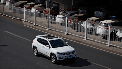 In this March 14, 2019, file photo, an SUV moves past dust-covered new Toyota cars stored underneath an overpass in Beijing. China's auto sales sank 5.4% in November from a year ago, putting the industry's biggest global market on track to shrink for a second year, an industry group reported Tues, Dec. 10, 2019. Drivers bought just over 2 million SUVs, sedans and minivans, according to the China Association of Automobile Manufacturers.