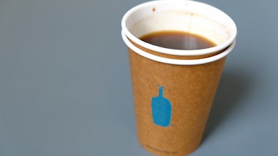 In this Thursday, Dec. 12, 2019 photo, a Blue Bottle Coffee paper to-go cup rests on a table outside one of their cafes in San Francisco. The Oakland-based chain says it's getting rid of disposable cups at two locations next year, as part of a pledge to go “zero-waste” at its 70 U.S. locations by the end of 2020.