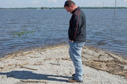In this May 10, 2019 photo, Brett Adams stands where the road to his flooded farm disappears under flood waters, with the farm buildings visible in the background, in Peru, Neb. Adams had thousands of acres under water, about 80 percent of his land, this year. The water split open his grain bins and submerged his parents' house and other buildings when the levee protecting the farm broke.