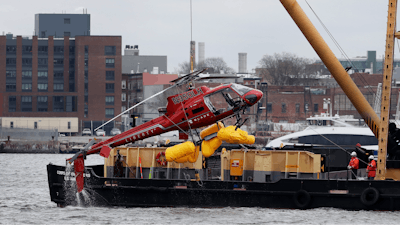 In this March 12, 2018 file photo, a helicopter is hoisted by crane from the East River onto a barge in New York. Federal investigators said Tuesday, Dec. 10, 2019, the helicopter company, whose doors-off flight crashed in a New York City river last year, exploited a regulatory loophole to avoid stricter safety requirements.