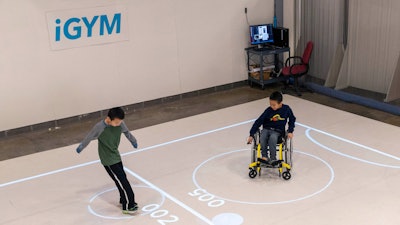 In this Nov. 17, 2019, photo provided by the University of Michigan, brothers Darren Kreps, left, and Bryan Kreps play a game modeled after soccer and air hockey using the iGYM system at the university in Ann Arbor, Mich. A University of Michigan research team has created iGYM, an augmented reality system that allows people with different levels of mobility to play and exercise together.