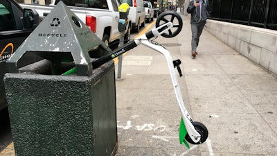 In this photo taken May 14, 2018, a man walks past an electric scooter that was dumped into a trash can in San Francisco. Tired of San Francisco streets being used as a testing ground for the latest delivery technology and transportation apps, city leaders are considering requiring businesses to get permits before trying out new high-tech ideas in public. Supporters of the legislation, which the Board of Supervisors will take up Tuesday, Dec. 10, 2019, say it would be the first of its kind in the U.S. They say it's long overdue in a city that's a hub for major tech companies but is more accustomed to reacting to the sudden arrival of new technology, such as when hundreds of dockless electric scooters appeared overnight last year.