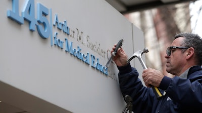 Worker Gabe Ryan removes a sign that includes the name Arthur M. Sackler at an entrance to Tufts School of Medicine, Thursday, Dec. 5, 2019, in Boston. Tufts University says it is stripping the Sackler name from its campus in recognition of the family's connection to the opioid crisis.