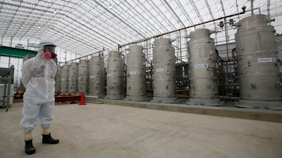 In this Nov. 12, 2014, file photo, a Tokyo Electric Power Co. (TEPCO) official wearing a radioactive protective gear stands in front of Advanced Liquid Processing Systems during a press tour at the Fukushima Dai-ichi nuclear power plant in Okuma, Fukushima Prefecture, northeastern Japan. Japan's economy and industry ministry has proposed gradually releasing or allowing to evaporate massive amounts of treated but still radioactive water at the tsunami-wrecked Fukushima nuclear plant. The proposal made Monday, Dec. 23, 2019, to a body of experts is the first time the ministry has narrowed down the options available to just releasing the water.