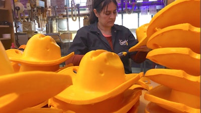 This Jan. 13, 2020 photo shows Maria Hernandez trimming foam cowboy hats at Foamation, Inc. in Milwaukee. Ralph Bruno invented the yellow wedge cheesehead in 1987 from his mother's couch stuffing and it has since become popular, particularly for Wisconsin sports fans and residents. His company, Foamation, Inc., which makes other foam products like these cowboy hats, moved into a new location in 2016 and soon started tours where people can make their own cheeseheads or other foam products.