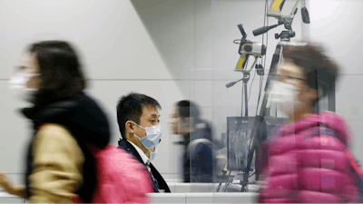 Passengers wearing masks walk by as a quarantine officer, center, monitors a thermography during a quarantine inspection at Kansai international airport in Osaka, western Japan, Wednesday, Jan. 22, 2020.