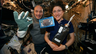 In this photo made available by U.S. astronaut Christina Koch via Twitter on Dec. 26, 2019, she and Italian astronaut Luca Parmitano pose for a photo with a cookie baked on the International Space Station. The results are finally in for the first chocolate chip cookie bake-off in space. While looking more or less normal, the best cookies required two hours of baking time last month up at the International Space Station. It takes far less time on Earth, under 20 minutes. And how do they taste? No one knows.