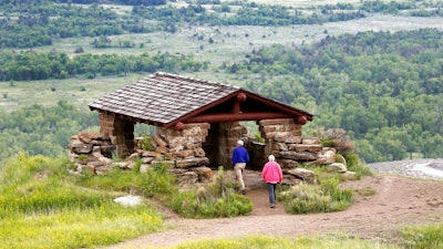 In this June 11, 2014, file photo, visitors hike to a stone lookout over the Little Missouri River inside the Theodore Roosevelt National Park, located in the Badlands of North Dakota. Anemic funding, alleged unpaid work and legal fights are hobbling developers of a proposed $800 million oil refinery near the park in western North Dakota. But the project manager for Meridian Energy Group's Davis Refinery, which has drawn criticism from environmental groups and others who worry it would add to pollution near the national park, insists it will be built.