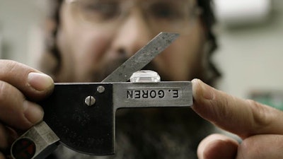 A diamond cutter displays a tool used to determine the angles of a large emerald cut diamond.