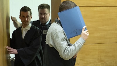 A 57-year old defendant hides his face at the courtroom in Bielefeld, Germany, Thursday, March 7, 2019. A judge in Germany has found the man guilty of poisoning his co-workers' sandwiches with mercury, lead acetate and other chemicals over several years and sentenced him to life in prison.