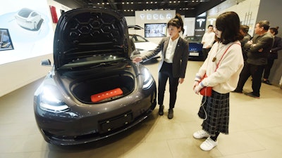 In this Nov. 24, 2019, photo, a saleswoman talks about a Tesla Model 3 car at a Tesla showroom in Hangzhou in eastern China's Zhejiang Province. Tesla's Shanghai factory delivered its first cars to customers Monday, Jan. 6, 2020, and chief executive Elon Musk said the electric automaker plans to set up a design center in China to create a model for worldwide sales.