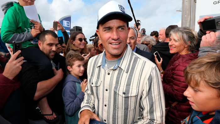 In this Oct. 9, 2019, file photo, surfer Kelly Slater is surrounded by fans after he leaves his footprint cement slab at Anglet Surf Avenue, in Anglet, southwestern France. Kelly Slater is planning to build the world's largest man-made wave in the desert. Plans for Coral Mountain will feature the largest, rideable, open-barrel human-made wave in the world with technology from Kelly Slater Wave Company, a division of the World Surf League. The wave basin will be part of a 400-acre site in La Quinta, California, set at the base of Coral Mountain.