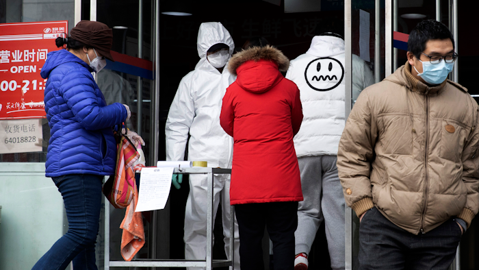A worker in overalls screen for fever at the entrance to a supermarket in Beijing Thursday, Feb. 27, 2020.