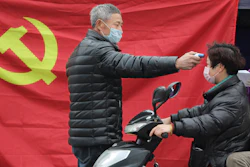 A volunteer stands in front of a Communist Party flag as he takes the temperature of a scooter driver at a roadside checkpoint in Hangzhou in eastern China's Zhejiang Province, Monday, Feb. 3, 2020.