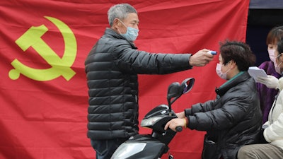 A volunteer stands in front of a Communist Party flag as he takes the temperature of a scooter driver at a roadside checkpoint in Hangzhou in eastern China's Zhejiang Province, Monday, Feb. 3, 2020.