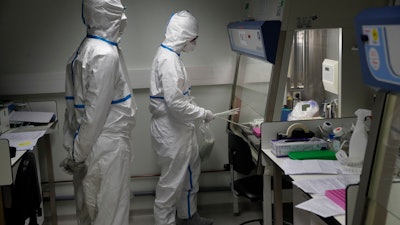 French lab scientists in hazmat gear inserting liquid in test tube manipulate potentially infected patient samples at Pasteur Institute in Paris, Thursday, Feb. 6, 2020. Scientists at the Pasteur Institute developed and shared a quick test for the new virus that is spreading worldwide, and are using genetic information about the coronavirus to develop a potential vaccine and treatments.