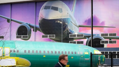 In this Dec. 16, 2019, file photo a Boeing worker walks past a 737 model fuselage and a giant mural of a jet on the side of the manufacturing building behind in Renton, Wash.