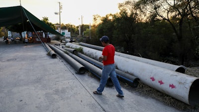 A man walks by pipes left on the ground after activists blocked the final meters construction of the thermo-electric plant pipeline in San Pedro Apatlaco, Morelos state, Mexico, Saturday, Feb. 22, 2020. The project has advanced in fits and starts for more than a decade. It's essentially complete, but legal stays have also prevented connection of the last mile of pipeline needed to fire up the power plant.
