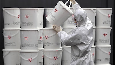 A worker in protective gear stacks plastic buckets containing medical waste from coronavirus patients at a medical center in Daegu, South Korea, Monday, Feb. 24, 2020. South Korea reported another large jump in new virus cases Monday a day after the the president called for 'unprecedented, powerful' steps to combat the outbreak that is increasingly confounding attempts to stop the spread.