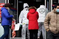 A worker in overalls screen for fever at the entrance to a supermarket in Beijing Thursday, Feb. 27, 2020.