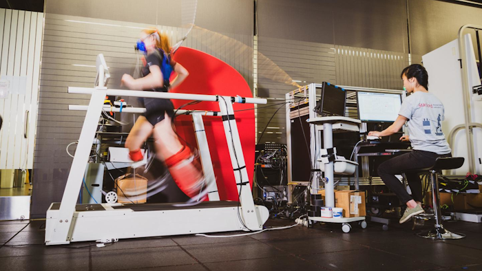 Graduate student Delaney Miller runs on a treadmill aided by the ankle exoskeleton emulator. Fellow graduate student Guan Rong Tan controls the emulator and monitors Miller's gait and respiration.
