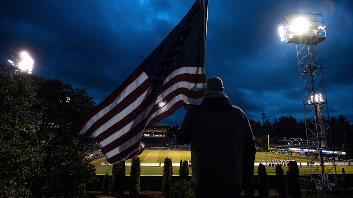 In this Wednesday, March 11, 2020 file photo, a man holds an U.S. flag as he watches the a United Soccer League match in Tacoma, Wash. In a matter of days, millions of Americans have seen their lives upended by measures to curb the spread of the new coronavirus in mid-March.