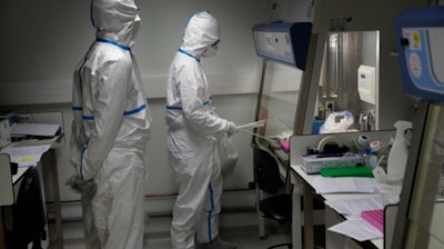 French lab scientists in hazmat gear inserting liquid in test tube manipulate potentially infected patient samples at Pasteur Institute in Paris, Thursday, Feb. 6, 2020.