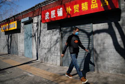 A man wearing a protective face mask walks by shuttered business shops in Beijing, Sunday, March 1, 2020. Amid fears about where the next outbreak of a fast-spreading new virus would appear, infections and deaths continued to rise across the globe Sunday, emptying streets of tourists and workers, shaking economies and rewriting the realities of daily life.