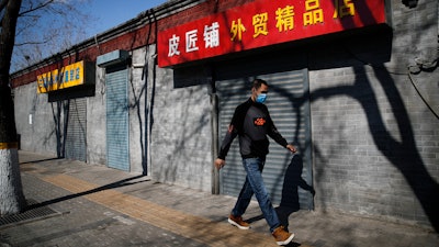 A man wearing a protective face mask walks by shuttered business shops in Beijing, Sunday, March 1, 2020. Amid fears about where the next outbreak of a fast-spreading new virus would appear, infections and deaths continued to rise across the globe Sunday, emptying streets of tourists and workers, shaking economies and rewriting the realities of daily life.