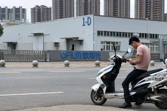 In this June 5, 2019, photo, a neighborhood resident stops for a smoke near the entrance to an OFILM factory in Nanchang in eastern China's Jiangxi province. The Associated Press has found that OFILM, a supplier of major multinational companies, employs Uighurs, an ethnic Turkic minority, under highly restrictive conditions, including not letting them leave the factory compound without a chaperone, worship, or wear headscarves.