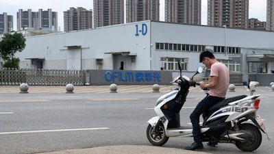 In this June 5, 2019, photo, a neighborhood resident stops for a smoke near the entrance to an OFILM factory in Nanchang in eastern China's Jiangxi province. The Associated Press has found that OFILM, a supplier of major multinational companies, employs Uighurs, an ethnic Turkic minority, under highly restrictive conditions, including not letting them leave the factory compound without a chaperone, worship, or wear headscarves.