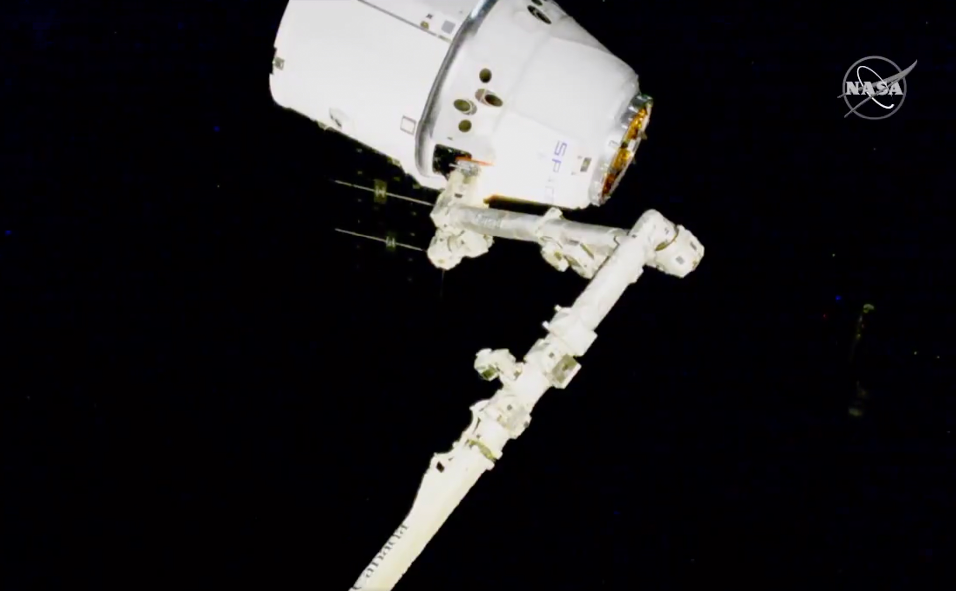 In this image taken from NASA video, NASA astronauts Andrew Morgan and Jessica Meir use the International Space Station's robot arm to capture the Dragon capsule Monday, March 9, 2020.