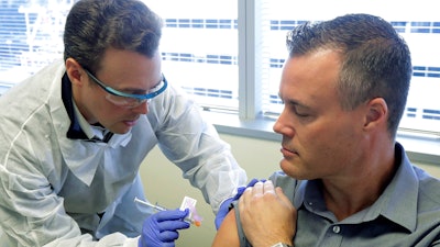 Pharmacist Michael Witte, left, gives Neal Browning a shot in the first-stage study of a potential coronavirus vaccine Monday, March 16, 2020, at the Kaiser Permanente Washington Health Research Institute in Seattle. Browning is the second patient to receive the shot in the study.