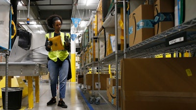 In this Dec. 17, 2019, file photo, Tahsha Sydnor stows packages into special containers after Amazon robots deliver separated packages by zip code at an Amazon warehouse facility in Goodyear, Ariz. On Monday, March 16, 2020, Amazon said that it needs to hire 100,000 people across the U.S. to keep up with a crush of orders as the coronavirus spreads and keeps more people at home, shopping online.