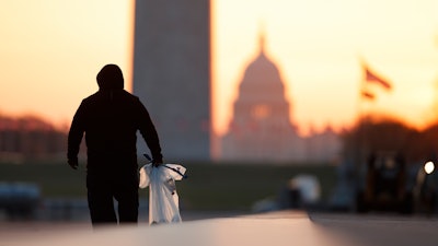 A National Park Service worker picks up trash along the drained Lincoln Memorial Reflecting Pool as the Washington Monument and the U.S. Capitol are seen in the distance in Washington, at sunrise Wednesday, March 18, 2020. The number of tourist is down ahead of an expected surge in coronavirus cases.