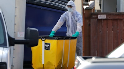 A member of a cleaning crew wheels a cart toward a vehicle at the Life Care Center, where at least 30 coronavirus deaths have been linked to the facility, Wednesday, March 18, 2020, in Kirkland, Wash. Staff members who worked while sick at multiple long-term care facilities contributed to the spread of COVID-19 among vulnerable elderly in the Seattle area, federal health officials said Wednesday.