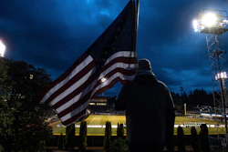 In this Wednesday, March 11, 2020 file photo, a man holds an U.S. flag as he watches the a United Soccer League match in Tacoma, Wash. In a matter of days, millions of Americans have seen their lives upended by measures to curb the spread of the new coronavirus in mid-March.